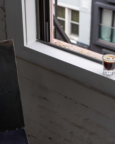 A lone espresso glass sits on an open windowsill 